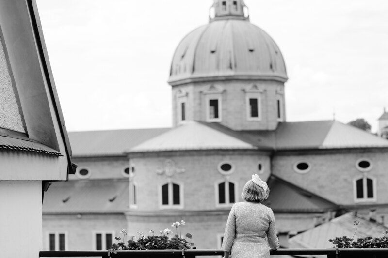 Wedding photography portfolio in Italy: A woman in a hat stands with her back on the balcony overlooking the large domes of the church