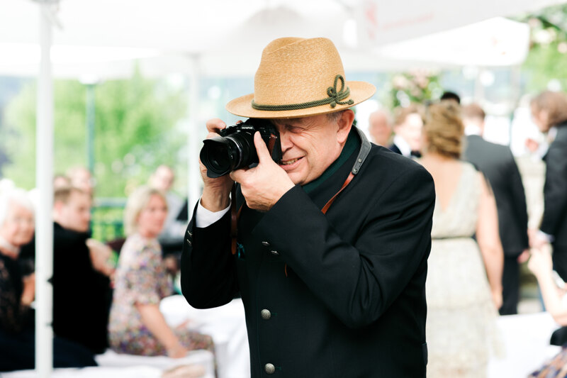 Wedding photography portfolio in Italy: A man in a black shirt and a straw hat photographs guests with his camera