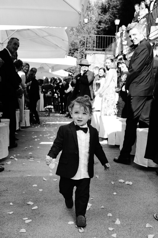 Wedding photography portfolio in Italy: Portrait of a little boy in a black tuxedo who sprinkles rose petals