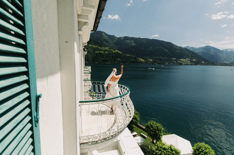 Wedding photography portfolio in Italy: The bride in a white dress stands on the balcony with a magnificent view of the lake and mountains