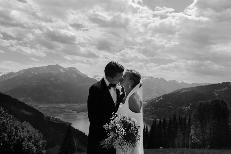 Wedding photography portfolio in Italy: A couple of newlyweds kiss in the valley against the backdrop of large mountains and a mountain lake