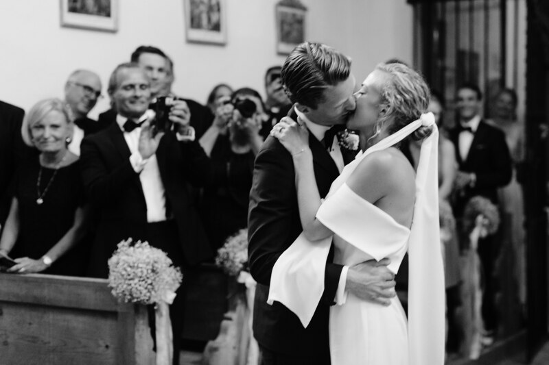 Wedding photography portfolio in Italy: A couple of newlyweds kiss in the church, guests greet them with applause and take pictures