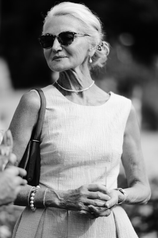 Wedding photography portfolio in Italy: Portrait of a beautiful, well-groomed elderly woman in a dress and black glasses, with a handbag on her shoulder and beads on her neck