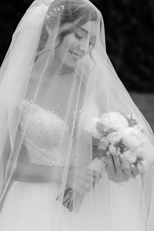 Wedding Photographer in Venice: A bride looks at a bouquet that she holds in her hands and smiles sweetly, her veil is easily covered by a veil
