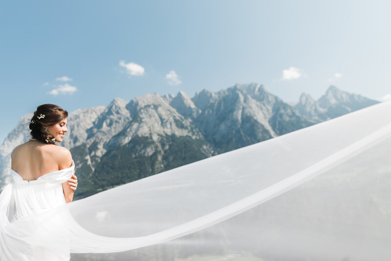 Wedding Photographer in Naples: The bride against the backdrop of luxurious mountains, the plume of her dress is widely dispelled by the wind, thereby emphasizing her fragile figure