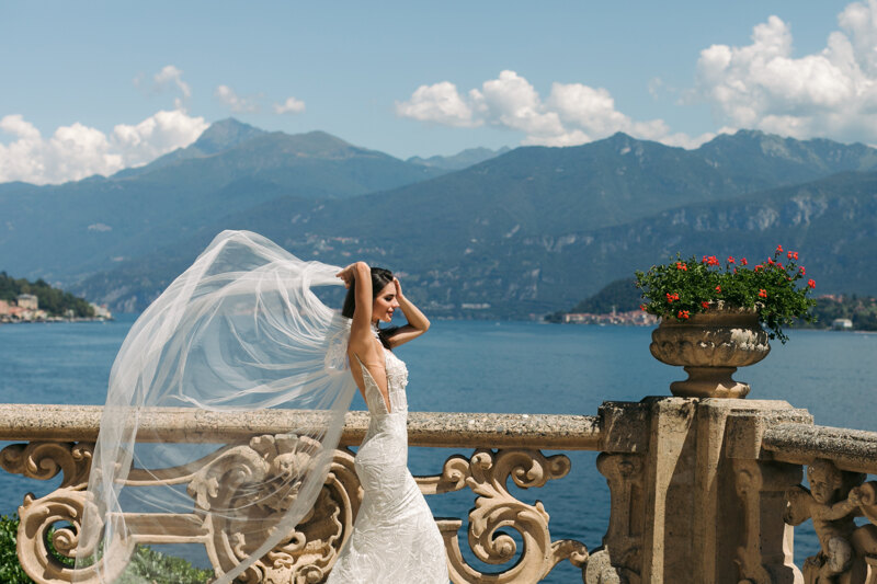  Wedding Photographer in Milan: Very beautiful bride, straightens her hair with her hand, against the backdrop of the sunny Lake Como