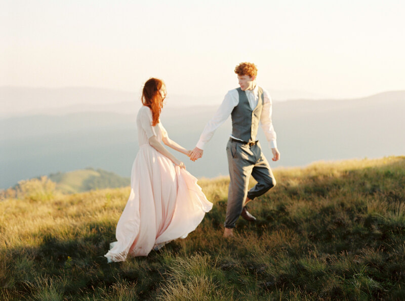 Wedding Photographer in Milan: An extraordinary couple of newlyweds with red hair, they walk along a sunny valley holding hands