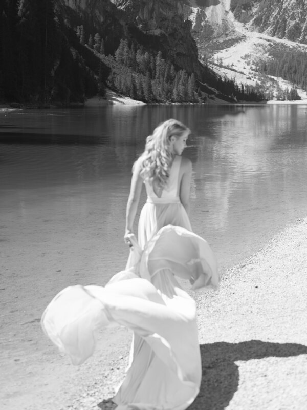 Wedding photography portfolio in Italy: A girl in a light airy dress walks against the backdrop of a mountain lake