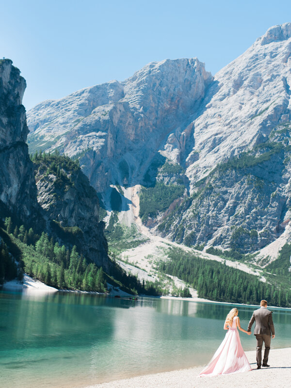 Wedding photography portfolio in Italy: Beautiful young couple walking holding hands by the lake in the mountains