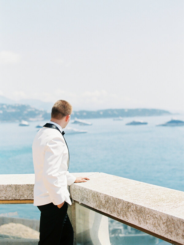 Wedding photography portfolio in Italy: The groom in a white tuxedo stands on the bridge and looks at the sea