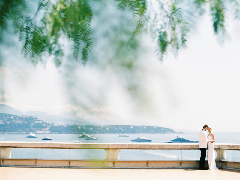 Wedding photography portfolio in Italy: Beautiful young newlywed couple standing cuddling on a bridge with sea view in Monaco