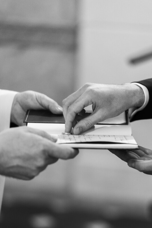 Wedding photography portfolio in Italy: The priest holds in his hands an open book on which lies the ring, the groom takes the ring in his hands to put it on his bride