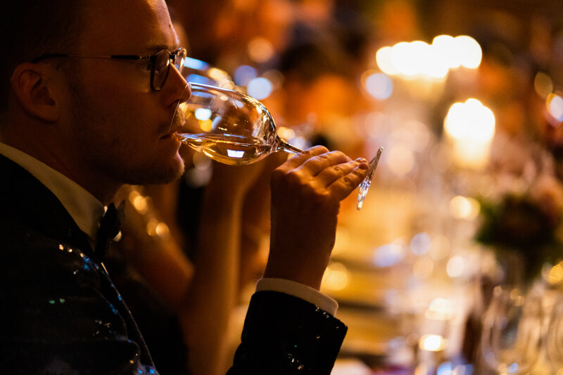 Wedding photography portfolio in Italy: Guest in a black suit and fashion glasses, drinking champagne