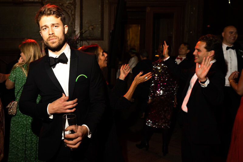 Wedding photography portfolio in Italy: A man is seriously looking into the frame, while guests are having fun and dancing nearby