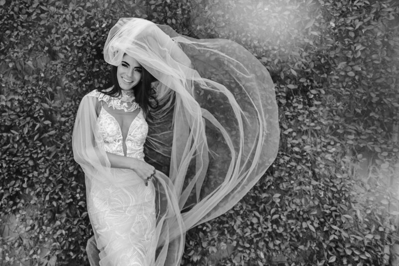 Couple photoshoot in Italy: Smiling bride in an incredibly beautiful wedding dress with a snow-white veil posing on the photographer’s camera