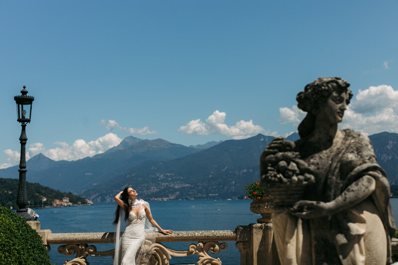 Couple photoshoot in Italy: A very beautiful bride, straightens her hair with her hand, against the backdrop of sunny Lake Como