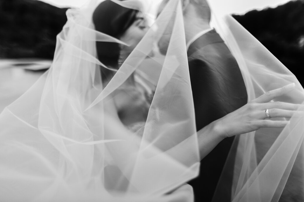 Couple photoshoot in Italy: Black-and-white frame where the bride and groom kiss and the wind wrapped them in a snow-white veil