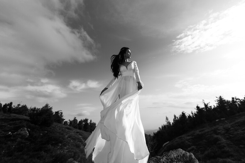 Couple photoshoot in Italy: A fragile bride, stands on a hill among the trees, catches the wind with her dress and hair