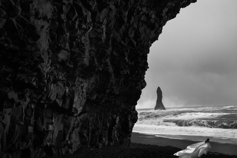 Couple photoshoot in Italy: A bold bride in a luxurious white dress with a wide train that dispels the wind on a black beach in Iceland