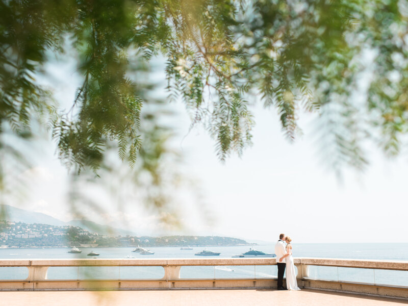 Couple photoshoot in Italy: An exquisite and luxurious couple of newlyweds who are hugging on the background of the coast in Monaco. Groom in a white tuxedo hugs his smiling bride, who is dressed in a designer wedding dress