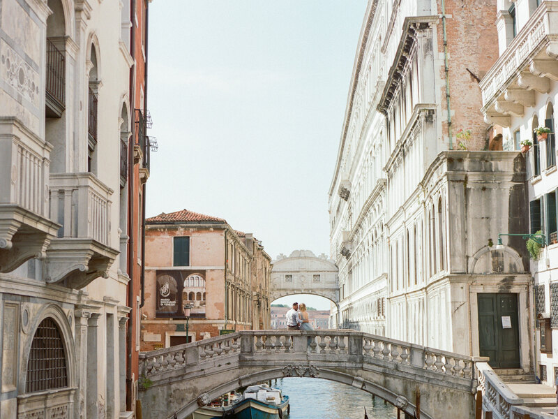 Couple photoshoot in Italy: Beautiful, young couple sitting and gently hugging on one of the bridges of romantic and sunny Venice