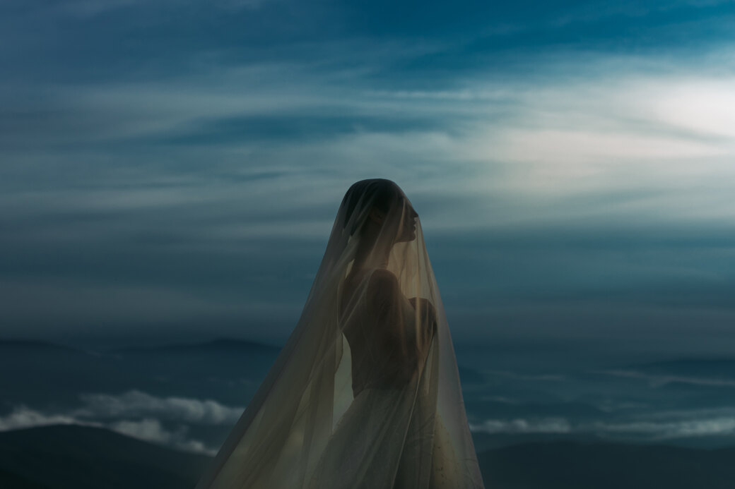 Wedding photography portfolio in Italy: Portrait of a bride in a wedding dress with a veil that covers her face, against a blue sky