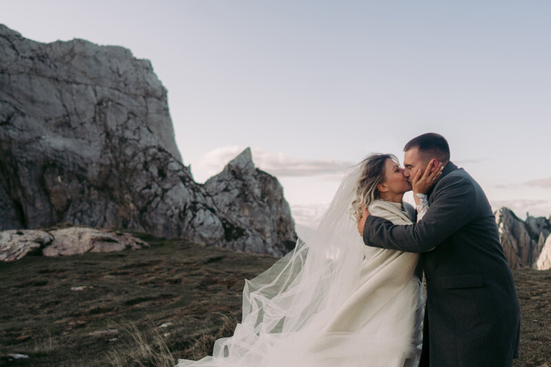 Wedding photography portfolio in Italy: Bride and groom kiss hotly high in the mountains, despite the strong wind and cold