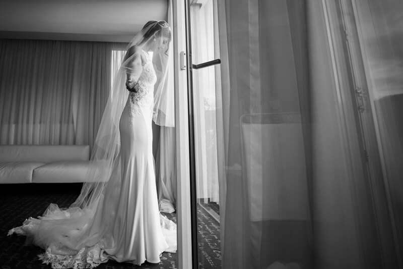 Wedding photography portfolio in Italy: A bride stands in front of a window in a hotel room, in a wedding dress, her face is covered by a translucent long veil