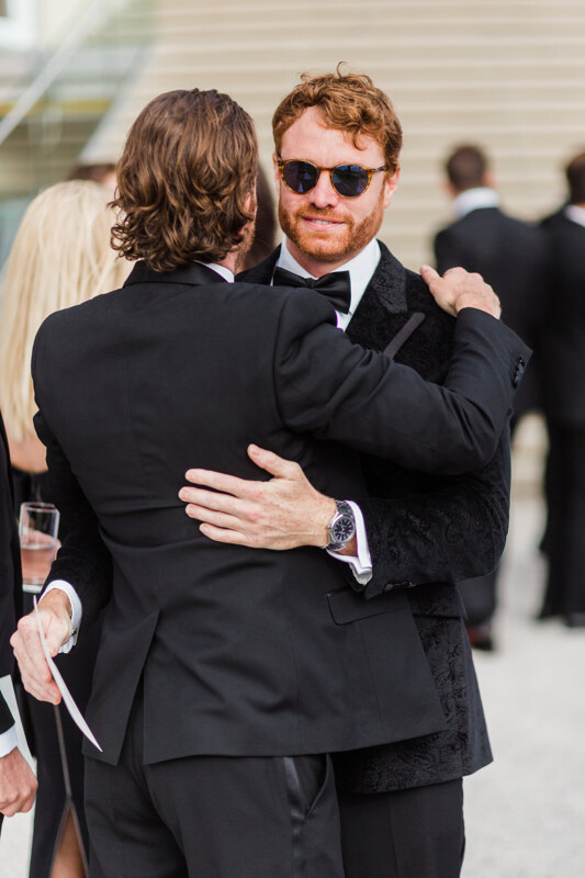 Wedding photography portfolio in Italy: Two men in tuxedos greeting each other hugging and shaking hands