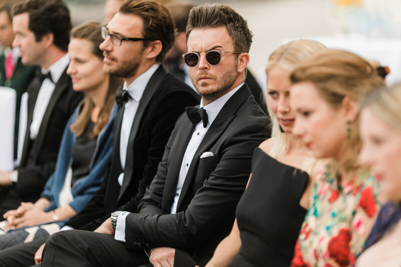 Wedding photography portfolio in Italy: A guest in a black tuxedo and black round glasses sits at a wedding ceremony