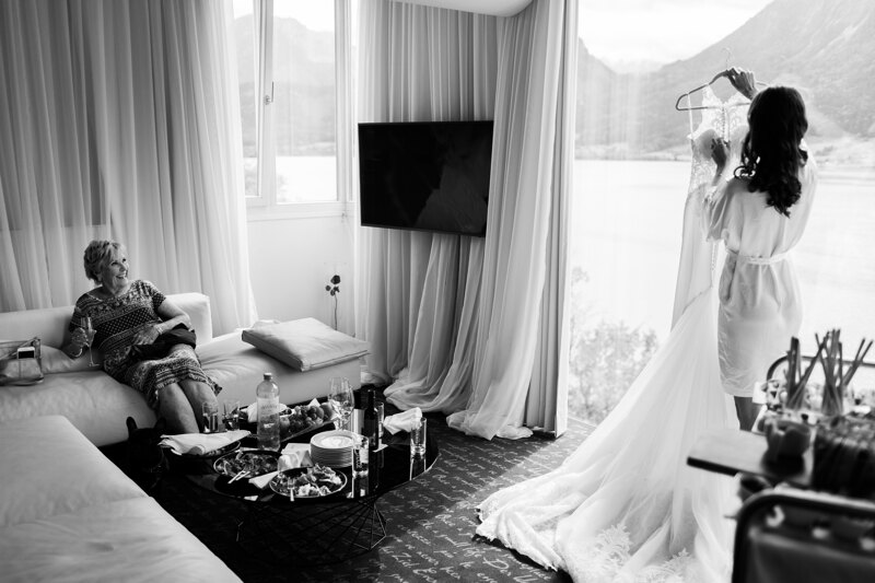 Wedding photography portfolio in Italy: Bride holds and examines her wedding dress in a hotel room with mountain and lake views