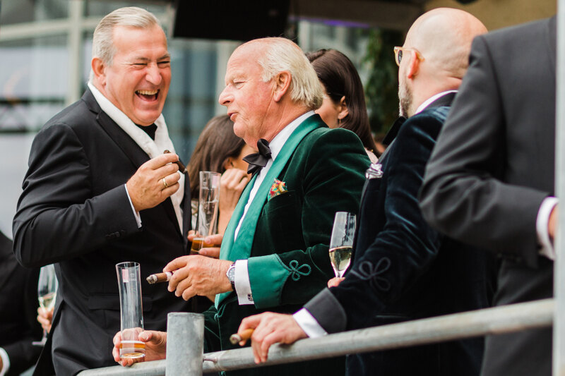 Wedding photography portfolio in Italy: Cheerful guests chatting with each other while drinking alcohol and smoking cigars