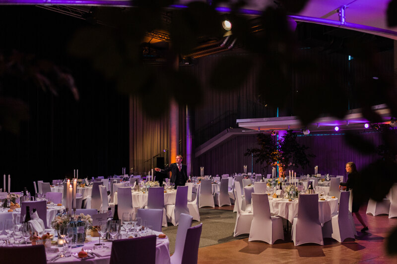 Wedding photography portfolio in Italy: A festive wedding hall, with round guest tables and white chairs that are illuminated by a professional light