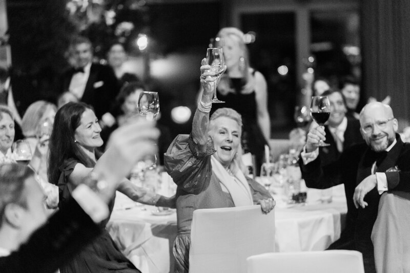 Wedding photography portfolio in Italy: Cheerful guests raise their glasses high while sitting at the table