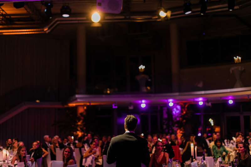Wedding photography portfolio in Italy: Groom says a toast to guests, looking at the festive hall